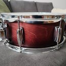 Kolaudovaný snare drum s tmavě hnědým dřevěným korpusem a chromovanými obručmi. Na mechanismu napnutí je viditelný nápis "Maestro". Nástroj vykazuje…