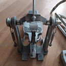 Kovový mechanismus pedálu, pravděpodobně basového bubnu. Povrch je stříbrný s viditelnými známkami opotřebení, škrábancemi a místními znečištěními. N…