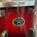 Červený buben s kovovým obručem a lugy. Na horním okraji je náleplka s nápisem Star-Mount, Star-Mount System TAMA. Uprostřed korpusu je oválný štítek…