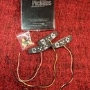 Sada dvou černých snímačů s nápisy LOLLAR TWEED a označením BRIDGE a NECK. K snímačům patří připojovací kabely a průhledný sáček s montážním přísluše…