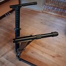 Černý kovový stojan na klavír nebo synthesizer s teleskopickými rameny. Na spodní části je viditelný nápis "KORG". Povrch je matný a vykazuje mírné z…