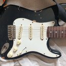Černá elektrická kytara typu Stratocaster s bílým pickguardem a hnědým hmatníkem. Na každém ze tří snímačů je nápis "Made in USA". Lak na těle kytary…