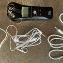 Černý digitální nahrávač s logem ZOOM a označením H1n. Vedle něj jsou položeny tři bílé kabely: napájecí kabel, sluchátka a audio kabel s 3,5mm konek…