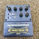 Modrý efekt pedál s nápisy HEAD RUSH a AKAI professional. Zařízení má několik ovládacích knoflíků, přepínačů a tlačítek s popisky jako MIX, HF DAMP,…