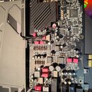 Fotografie zobrazuje elektronickou základní desku s černým plošným spojem, osazenou kondenzátory, rezistory a integrovanými obvody. Na desce je umíst…