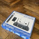 Krabice s bezdrátovým mikrofonním systémem značky skytec. Na obalu je nápis STWM722C MICRO UHF 2CH COMBI a adresa www.tronios.com. Fotografie na krab…