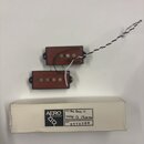 Dvě humbuckery s černým rámečkem a hnědými cívkami, z nichž jeden má připojený bílo-černý pletený kabel. Pod snímači je bílý papírový obal s nápisy A…