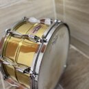 Zlatý kovový buben s chromovanými obručemi a napínacími šrouby. Na bílé bláně je viditelné logo značky GRETSCH. Povrch bubnu vykazuje drobné škrábanc…