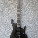 Černá elektrická kytara s matným povrchem a ostře hranatým tvarem těla. Nástroj má dva humbuckery, jeden ovládací knoflík hlasitosti a hmatník bez vi…