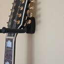 Černá hlava kytary s nápisem GRETSCH a zlatými ladičkami. Nástroj visí na černém nástěnném držáku. Na hmatníku jsou viditelné bílé vložky ve tvaru ko…