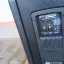 Zadní strana černého reproduktoru s texturou povrchu. Na ovládacím panelu je nápis db SUB 280 a označení výstupů OUT 1 a OUT 2. Jsou zde vidět čtyři…