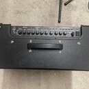 Černý kytarový kombo zesilovač s texturovaným povrchem a kovovými rohy. Na ovládacím panelu je logo ROLAND a nápisy AMPLIFIER, EQUALIZER a EFFECTS. N…