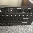 Černý rackový audio přístroj s řadou vstupů a výstupů. Na horní části jsou nápisy Phones, Tape In (s konektory L a R), Mono Output s ovladačem Level…