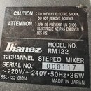 Fotografie detailu černé štítku na zařízení. Je na něm uveden název značky Ibanez a MODEL NO. RM122, s popisem 12CHANNEL STEREO MIXER. Štítek obsahuj…