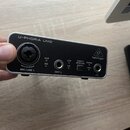 Stříbrný audio rozhraní s nápisem U-PHORIA UM2 a logem behringer. Zařízení obsahuje vstup MIC/LINE 1 s XLR konektorem, vstup INST 2 a výstup pro sluc…