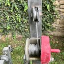 Detail kovové konstrukce s mechanismem z ocelového lana. Součástí je navíječka s červeným plastovým krytem a klikou, která vede přes horní kladu. Pov…