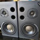 Dva šedé studiové reproduktory značky Alesis. Každý obsahuje jeden výškovej reproduktor, dva bassreflexní otvory a jeden basový reproduktor s nápisem…