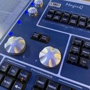 Detailní pohled na modré ovládací pult s nápisem MagicQ. Jsou zde vidět dvě stříbrné vrutové ovratovky označené X a Y, dva menší stříbrné knoflíky a…