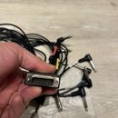 Fotografie zachycuje svazku černých kabelů zakončených několika 6,3mm jack konektory. V popředí drží ruka jeden z konců kabelu s vícepinovým D-Sub ko…