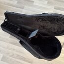 Otevřený černý pol pevný pouzdro na kytaru s vnitřním čalouněním z černého plyšového materiálu. V horní části vnitřku je umístěn malý černý předmět s…