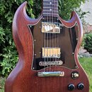 Hnědá elektrická kytara s charakteristickým tvarem SG a tmavým hnedým pickguardem. Nástroj má dva humbuckery, čtyři ovládací knoflíky a jeden přepína…
