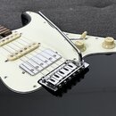 Detail elektrické kytary s černým bodies a bílým pickguardem. Na instrumentu jsou vidět dva snímače, chromovaný most s páčkou a dva ovládací knofíky…