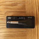 Černý plastový adaptér s připojeným kabelem a konektorem. Na povrchu je bílý nápis BATTERY: AAA SIZE (R03, LR03) X 2 (3V), logo VOX, značky CE a text…