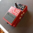 Červený kytarový pedál značky BOSS s nápisem Loop Station RC-3. Na horní straně jsou ovládací prvky, přepínače a displej s nápisy jako MEMORY, RHYTHM…
