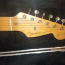 Hlava elektrické kytary v přirozené dřevěné barvě s šesti ladicími kolíky. Na dřevě je černý nápis Fender STRATOCASTER a pod ním menší text WITH SYNC…