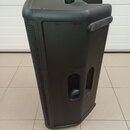 Černý plastový aktivní reproduktor s mřížkou na přední straně. Má integrovanou rukojeť nahoře a na boku, v dolní části je otvor pro umístění na stoja…