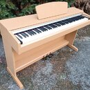 Digitální piano v dřevěné barvě s bílými a černými klávesami. Nástroj má integrovaný podstavec se třemi pedály a nad klaviaturou je umístěn jednoduch…