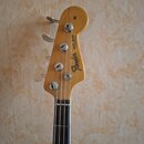 Fotografie zachycuje hlavu basové kytary v přírodním dřevě. Na povrchu je černý nápis Fender a vedle něj text JAZZ BASS ELECTRIC BASS oraz MADE IN US…