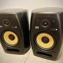 Dva černé studiové monitory s žlutými membránami basových reproduktorů. Na přední straně každého z nich je zlaté logo KRK a bílý nápis VXT8. Povrch j…