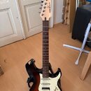 Elektrická kytara s tmavě hnědým sunburst povrchem těla a bílým pickguardem. Na světlé hlavě je viditelné logo Yamaha v kroužku a nápis PACIFICA. Hри…