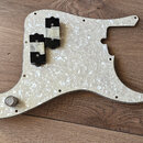 Bílá perleťová pickguard pro elektrickou kytaru s dvěma černými humbuckery. Snímače jsou připevněny k povrchu pomocí bílé lepicí pásky. V dolní části…