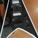 Černá elektrická kytara s bílým lemováním v tvaru V. Na hmatníku jsou vidět dva humbuckery s nápisem jackson a černý most s nápisem Jackson. Kytara m…