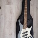 Šedá elektrická basová kytara s bílým pickguardem a hnědým hmatníkem, položená na černém softcasu. Na hlavě nástroje je viditelné logo značky Ibanez.…