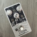 Bílý kytarový efekt s černým grafickým motivem krajiny. Na šasi jsou čtyři bílé otočné knoflíky s popisky Tone, Volume, Gain a Bandwidth, přepínač Vo…