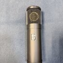 Kondenzátorový mikrofon s matně černým kovovým tělem a mřížkovou hlavicí. Uprostřed těla je umístěno stříbrné logo ve tvaru stylizovaného písmene S.…