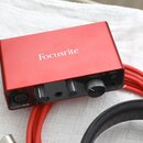 Červené audio rozhraní značky Focusrite. Na přední straně jsou umístěny dva otočné knoflíky, jeden větší knoflík s nápisem MONITOR a vstup XLR. V lev…