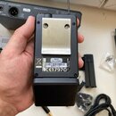 Černý bezdrátový vysílač typu beltpack s kovovým stříbrným klipem. Na zadní straně je bílá nálepka s nápisy: BELTPACK TRANSMITTER MODEL C88, FREQ: 60…