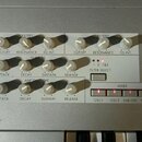Detailní pohled na ovládací panel syntetizátoru s šedým povrchem. Panel obsahuje sekce FILTER 1, FILTER EG a AMP ENVELOPE s bílými otočnými knoflíky,…