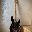 Elektrická basová kytara s černým tělem a přechodem do hnědé v oblasti středu. Na hlavě je viditelné logo "Squier". Nástroj má světle hnědý hmatník a…