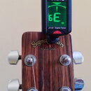 Na hlavě kytary z tmavého dřeva je nápis Sigma Guitars a pod ním EST.1970. Na hlavě je upevněn černý digitální ladička značky JOYO s označením JT-07…