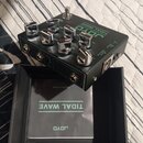 Černý kytarový efekt s nápisem JOYO TIDAL WAVE a chromovanými ovládacími knoflíky. Na boku jsou viditelné vstupy OUTPUT a DC 9V. Nástroj leží v černé…