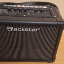 Černý kytarový kombo zesilovač s mřížkou reproduktoru v přední části. Na mřížce je bílý nápis Blackstar. Horní ovládací panel obsahuje několik potenc…