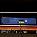 Modré rackové zařízení MIDAS DL153 audio system I/O umístěné v hliníkovém přepravním kufru. Na přední straně je žlutá nálepka s nápisem ID 2, několik…