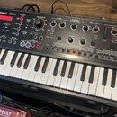 Černý syntezátor s klaviatura značky Roland, model JD-Xi. Horní panel obsahuje červený displej, početné ovládací knofíky a tlačítka rozdělená do sekc…