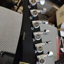 Záběr na zadní stranu černé hlavy kytary s šesti chromovanými ladicími mechanismy. Na každém mechanismu je nápis G GOTOH JAPAN BRIDGE LOCKS a NARROW…