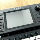 Černý hudební sampler s displejem a ovládacími prvky. V horní části je bílý nápis AKAI PROFESSIONAL. Na pravé straně se nachází otočný knoflík a čtyř…